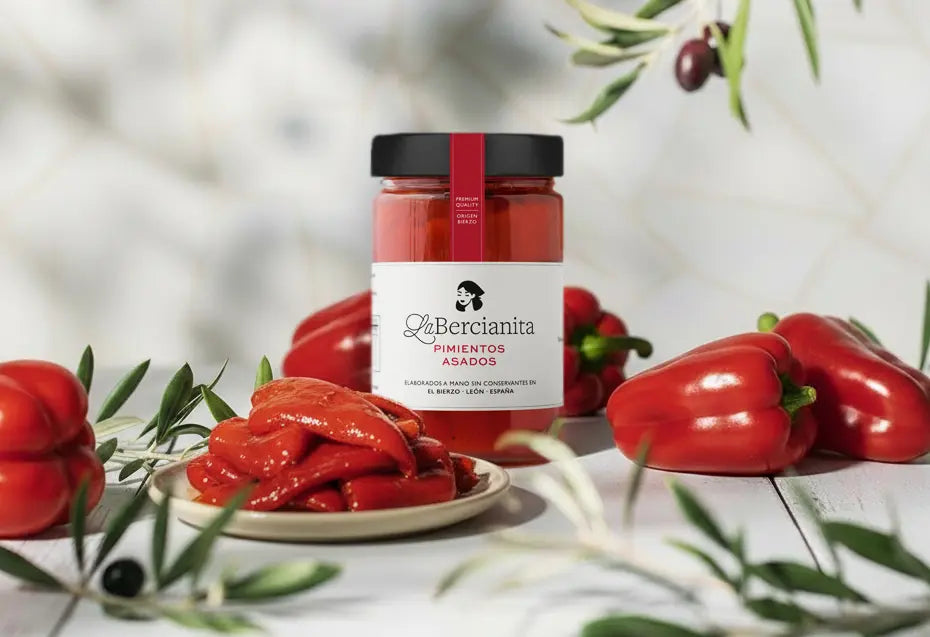 Bote grande de pimientos asados del Bierzo La Bercianita junto a pimientos frescos y servidos sobre fondo blanco